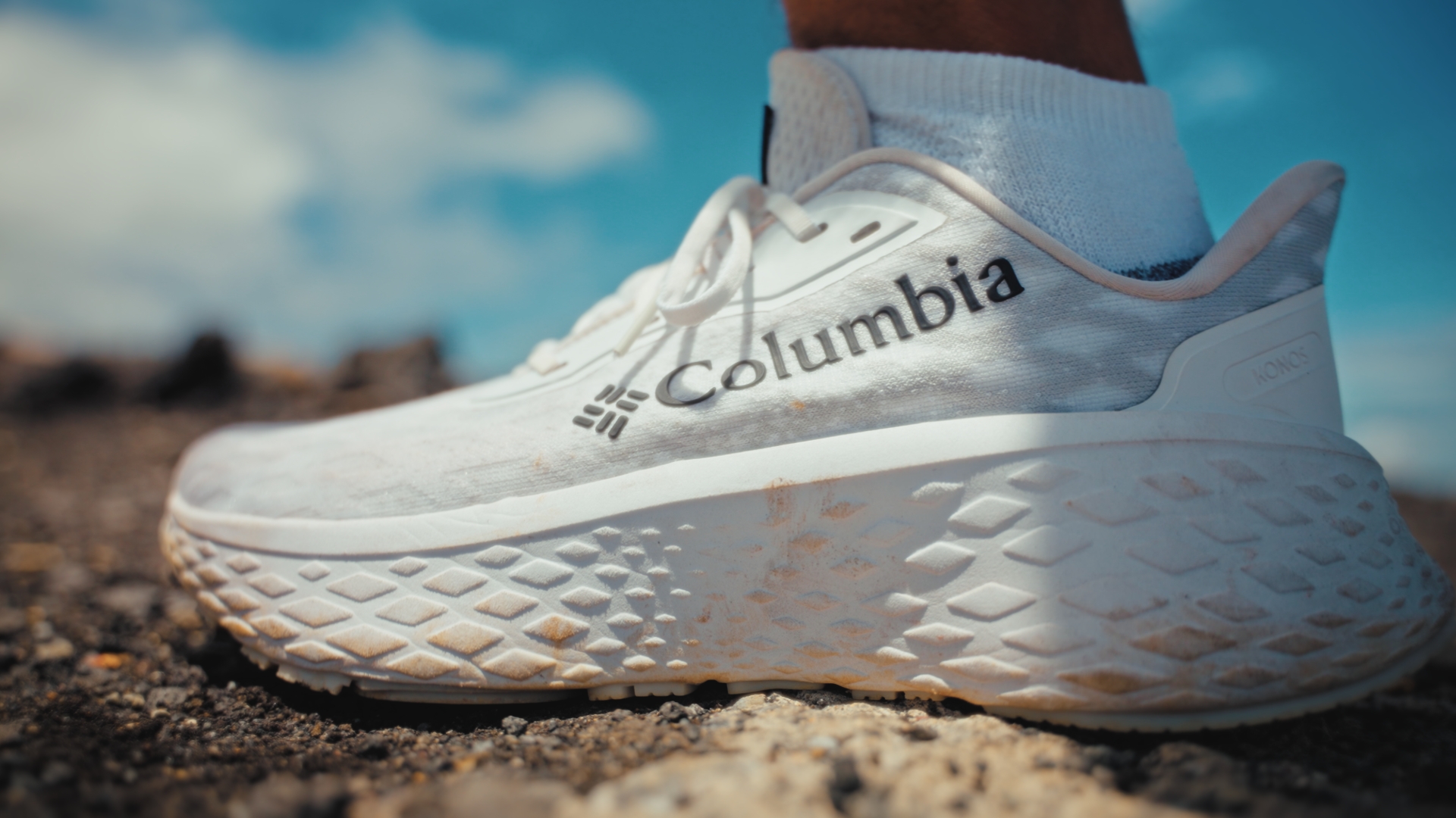 Close-up of a Columbia running shoe on rocky ground under a blue sky