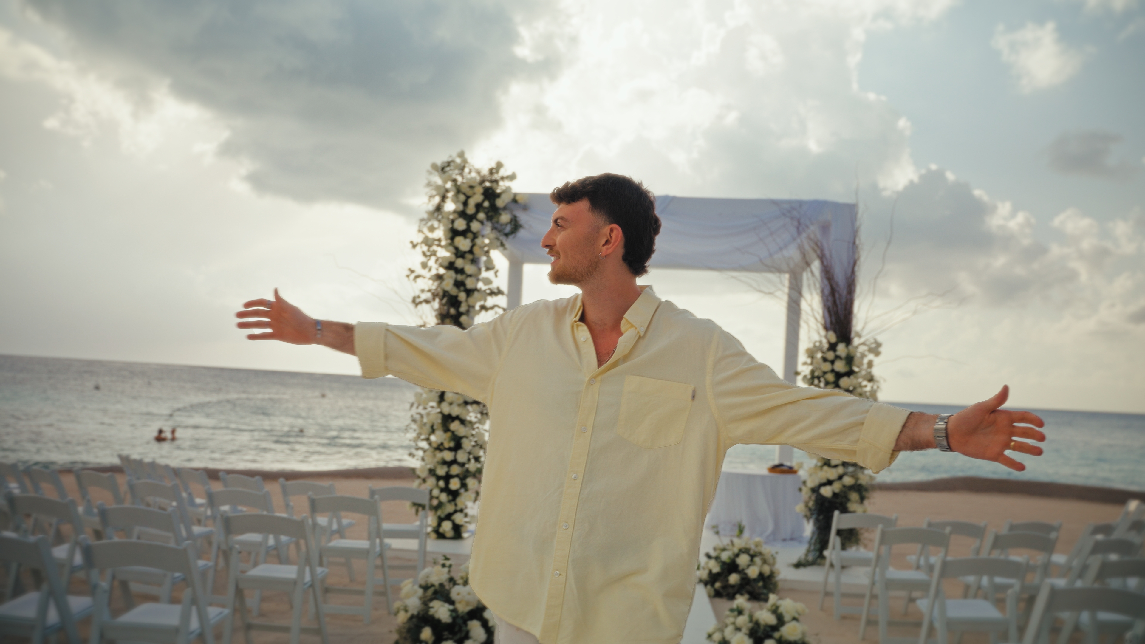 A person with arms open at a beachside ceremony at dusk